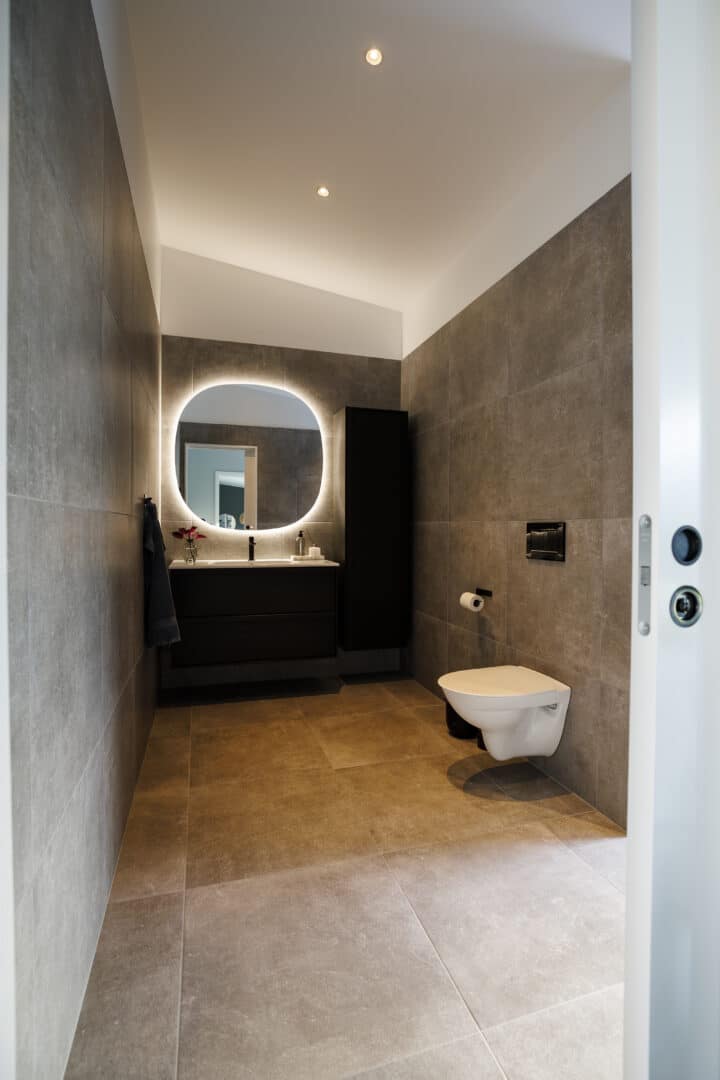 Toilet with grey tiles and black bathroom furniture.