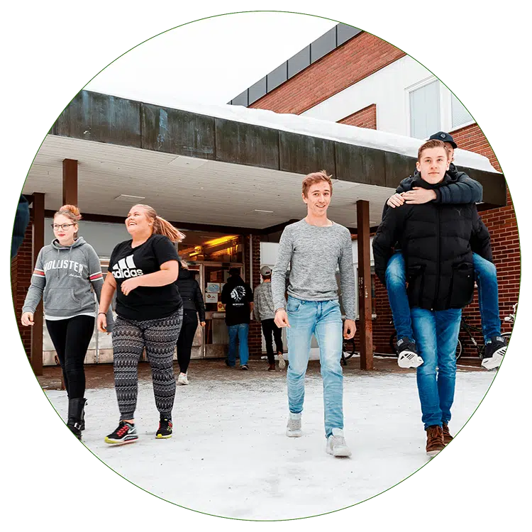 Fyra ungdomar i jeans och mörka tröjor går framför en tegelbyggnad på en skolgård.
