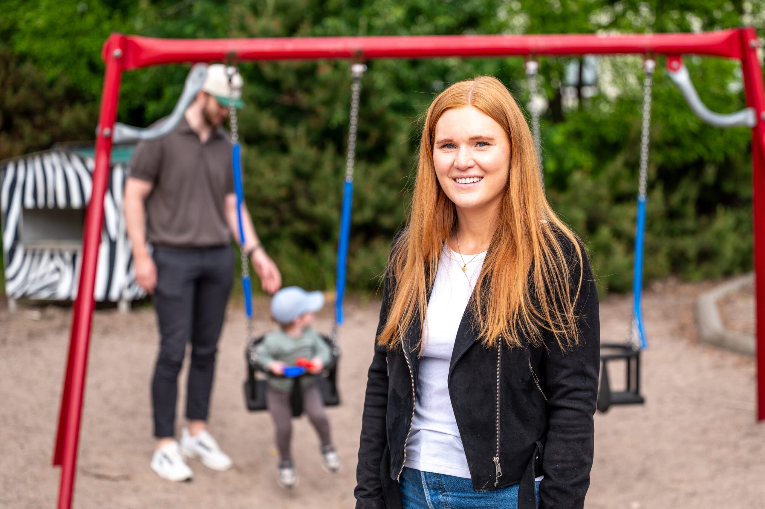 En kvinna med långt rött hår står i förgrunden med en man och ett barn i bakgrunden